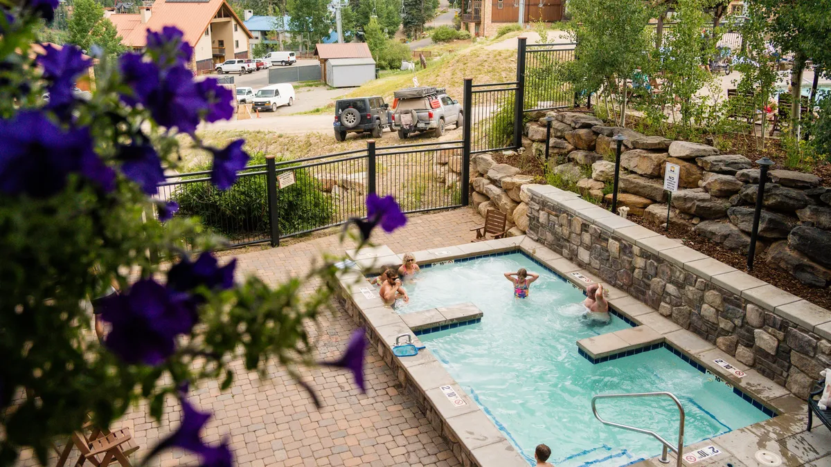 A lively outdoor swimming pool scene with children playing in the water, surrounded by blooming flowers. The pool area is designed for fun, relaxation, and socializing, capturing the family-friendly and energetic resort atmosphere.
