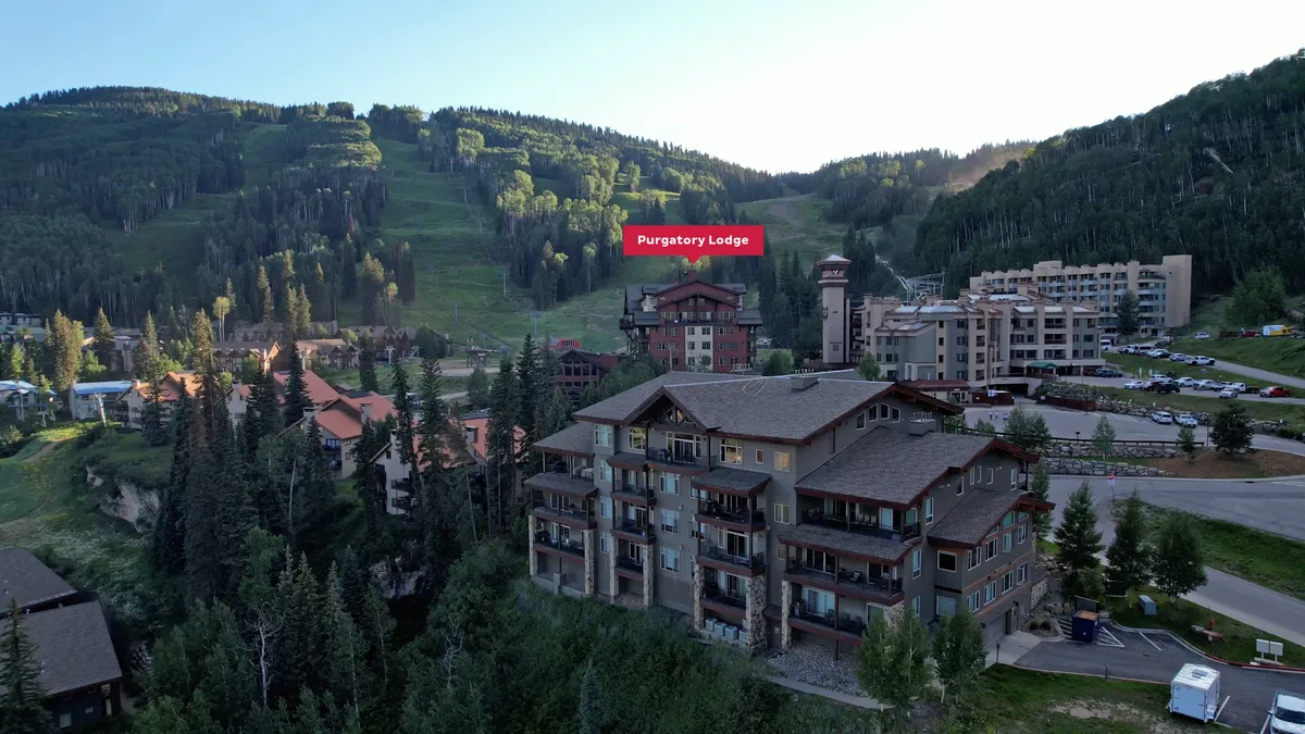 An exterior perspective of Purgatory Lodge and its neighboring resort buildings, with expansive mountain vistas, a visible parking area, and multiple balconies. The image demonstrates the central location and the social, communal aspect of the village.