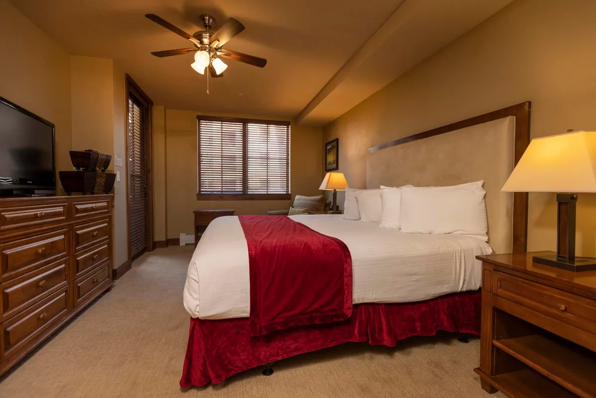 A serene bedroom featuring a plush bed with soft bedding, a nightstand lamp casting a gentle glow, a window letting in morning light, and a dresser for storage. The space is uncluttered, comfortable, and inviting, perfect for restful sleep and quiet moments.