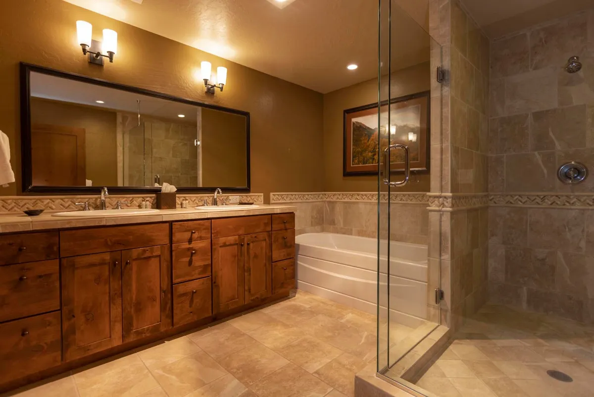 A spacious, well-appointed bathroom with a double vanity, large mirror, glass-enclosed shower, and a bathtub. The mood is calm and rejuvenating, with plenty of space for self-care and refreshing after outdoor activities.