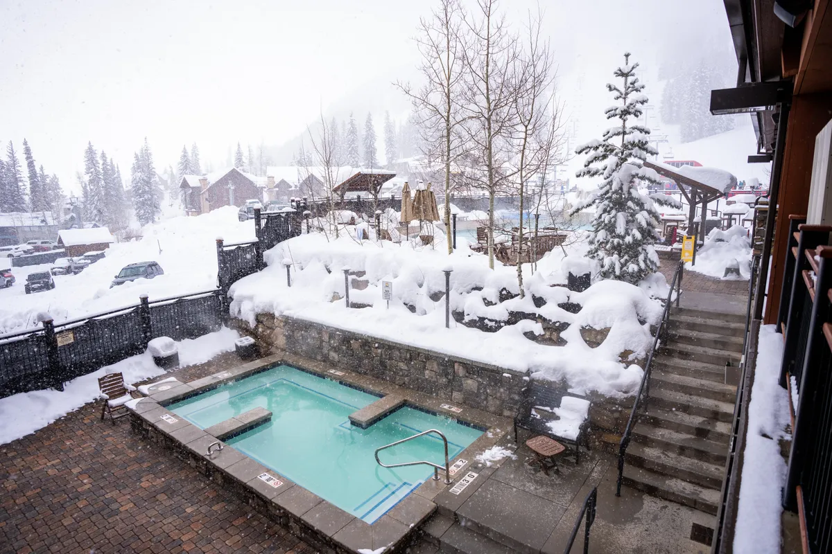 An inviting hot tub nestled amidst a snow-covered landscape, surrounded by pine trees and stone accents. Steam rises from the warm water, creating a tranquil oasis for relaxation even in wintery conditions.