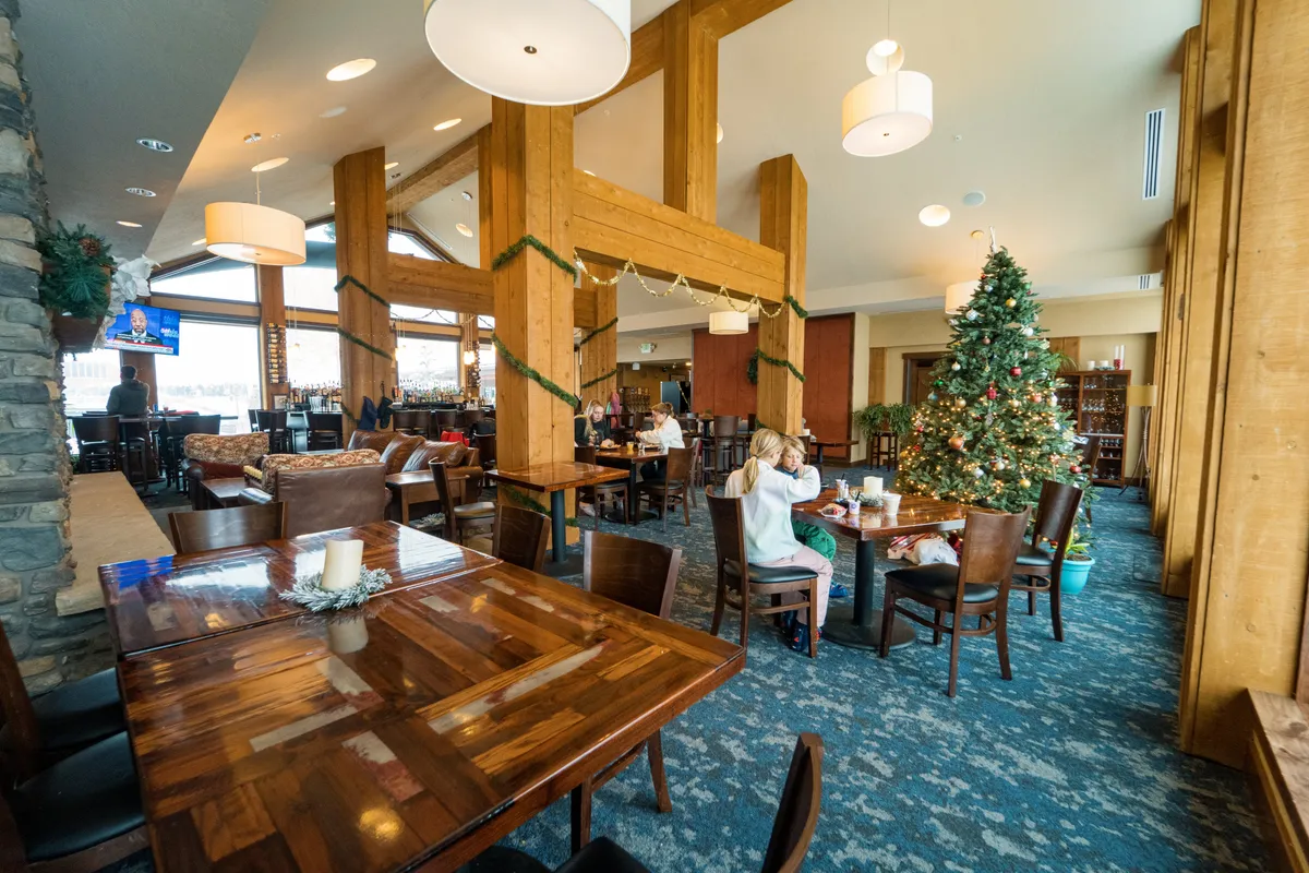 This lively interior scene captures Purgy’s Restaurant and Bar at its coziest, with large wooden beams, a festive Christmas tree, tables full of diners, and a welcoming bar area glowing in the background. The overall atmosphere is warm and bustling, perfect for après-ski celebrations or family gatherings.