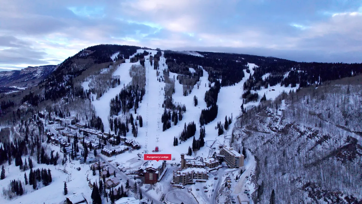 This image captures Purgatory Lodge at the foot of snow-covered slopes, surrounded by trees and mountains, immersed in a pristine winter setting. The lodge is clearly positioned for direct access to the slopes, emphasizing its ski-in/ski-out convenience.