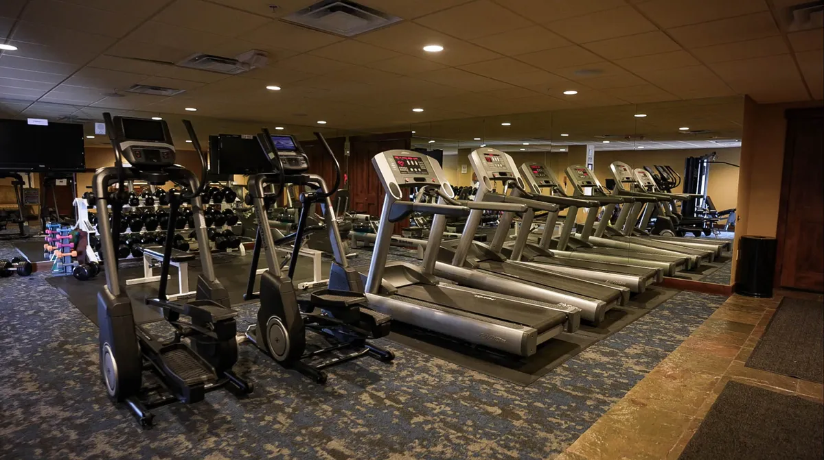A well-equipped fitness center featuring treadmills, elliptical machines, free weights, mirrored walls, and televisions. The setting is modern and energizing, ideal for workouts and group fitness activities.